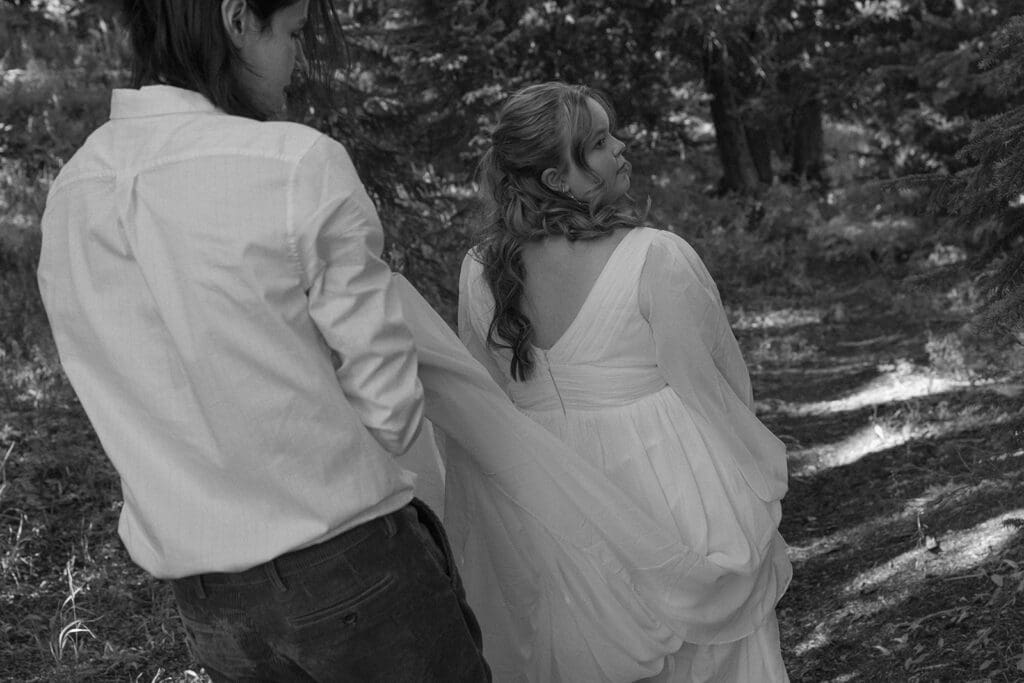 Black and white image of bride looking over her shoulder as her husband gently holds her dress during their intimate Crested Butte elopement in the woods.