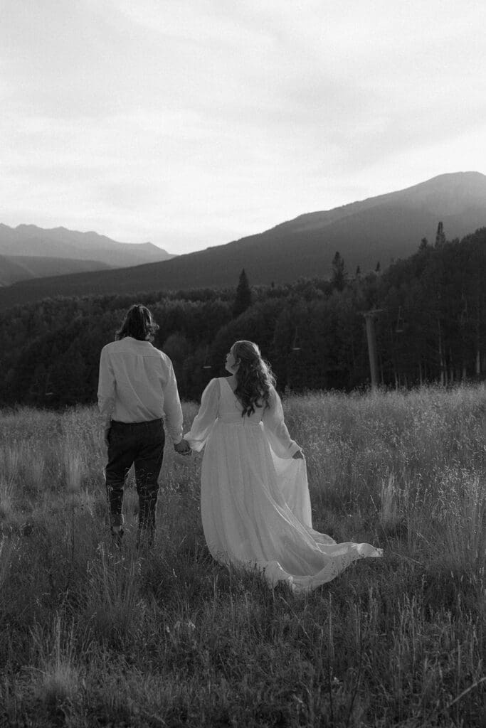Black and white photo of a couple walking hand in hand through a mountain meadow in Crested Butte, highlighting documentary elopement photography and intimate Colorado wedding moments.