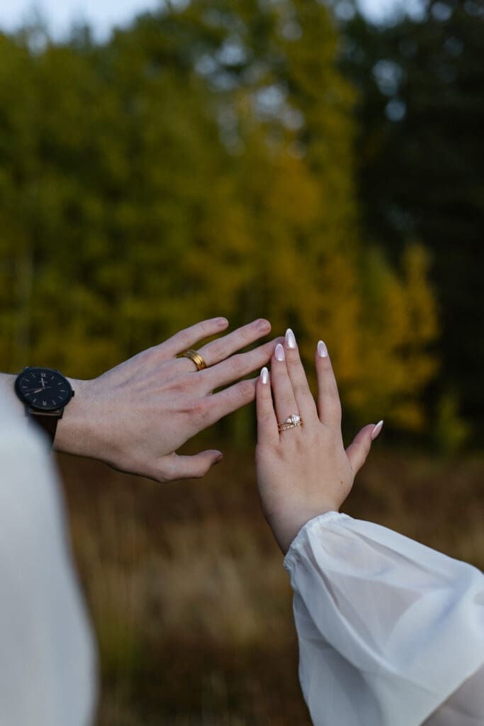 The groom's hand and bride's hand showing off their new wedding rings after having eloped in Crested Butte, Colorado.