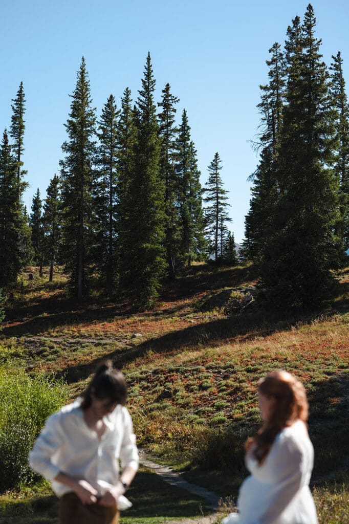 Couple adjusting their outfits on a mountain trail during their Crested Butte elopement, surrounded by forest and alpine scenery.