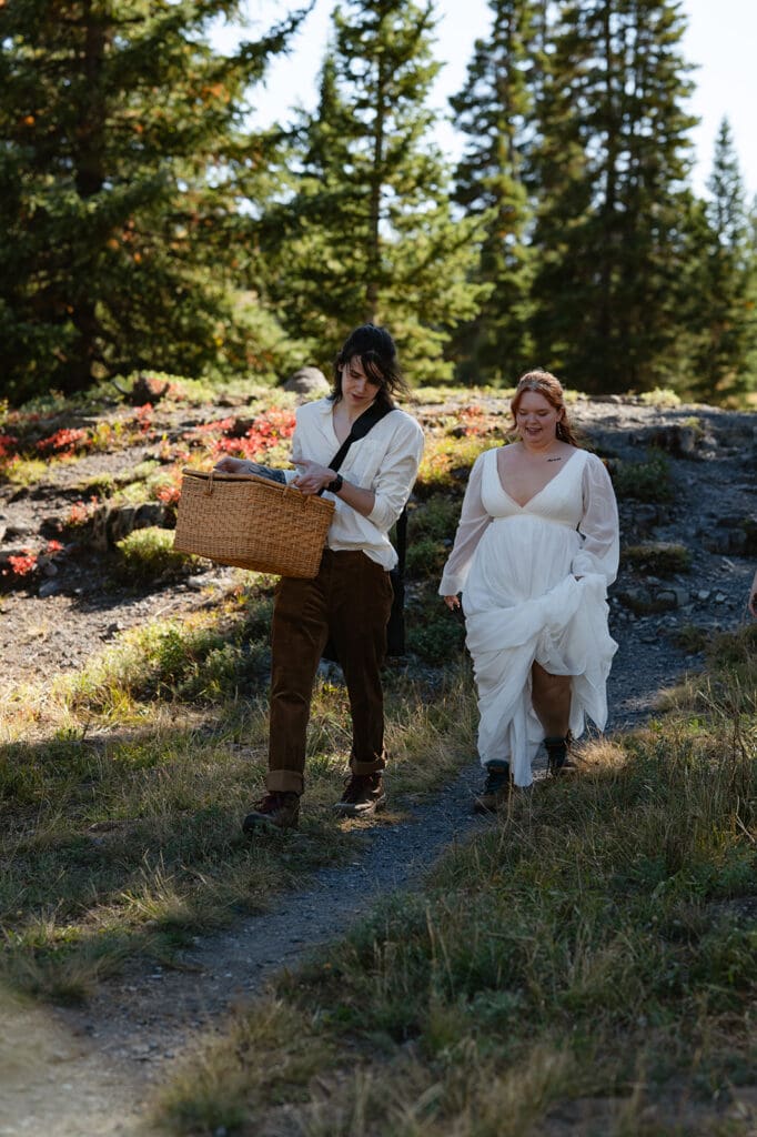 Couple walking along a rocky mountain path during their Crested Butte elopement with evergreen trees and blue sky behind them.