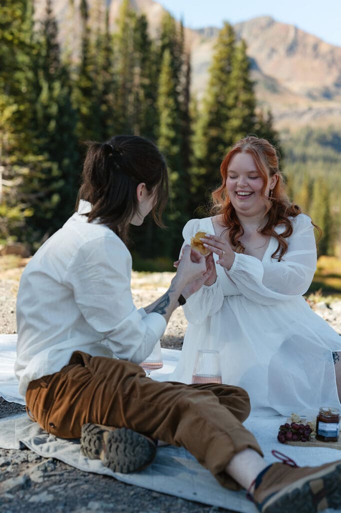 Couple laughing together on a mountain picnic during their Crested Butte elopement, surrounded by pine trees and alpine views.
