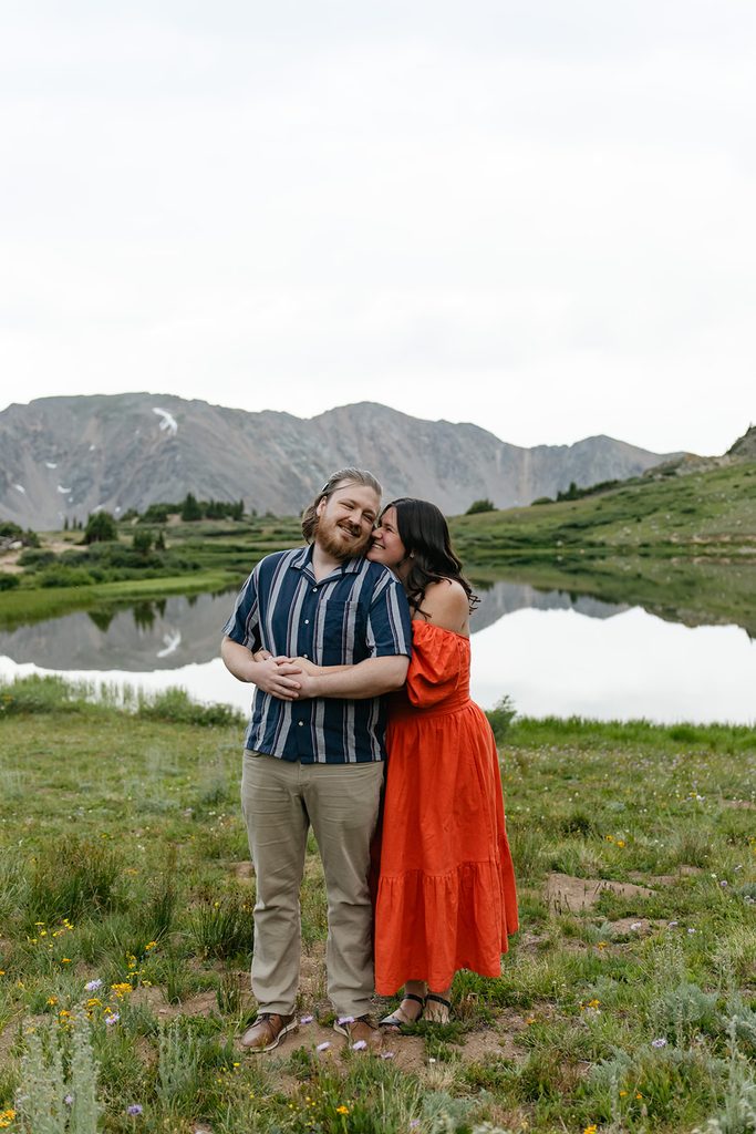 a girl in an orange dress nuzzles into her fiance's neck for engagement photos at Pass Lake
