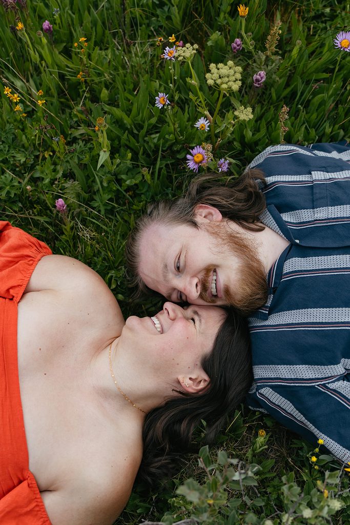 a couple lay in the grass, nose to nose, with wildflowers around them
