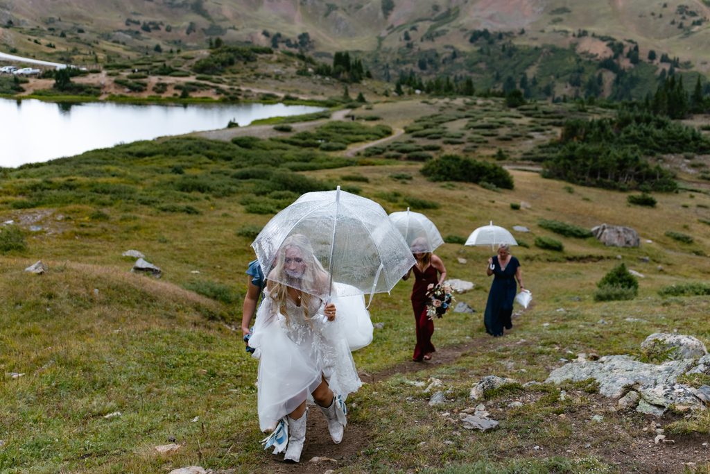 a bride and her moms walk up the hill at pass lake holding clear umbrellas at Pass Lake