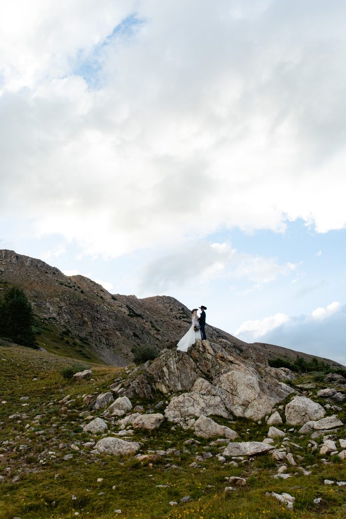 A wide shot of a bride and groom standing on a rock outcropping at pass lake