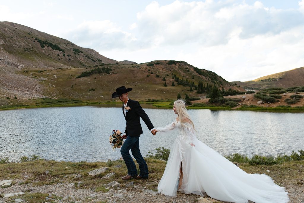 a groom takes his bride's hand and leads her down the path near Pass Lake
