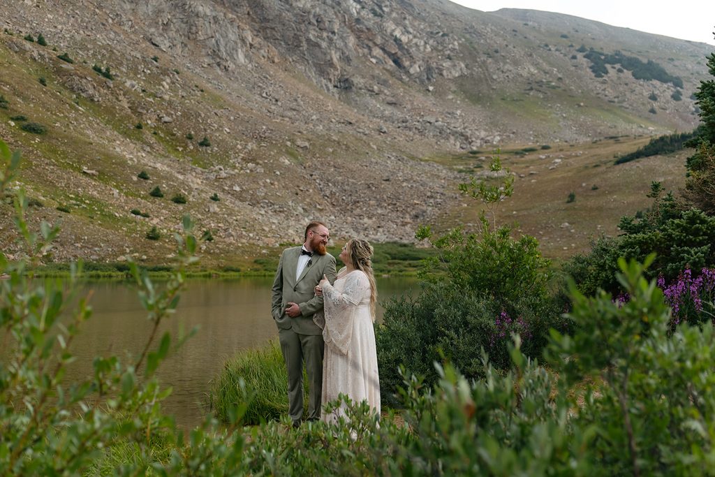 a couple stands arm in arm among the green foliage at Pass Lake