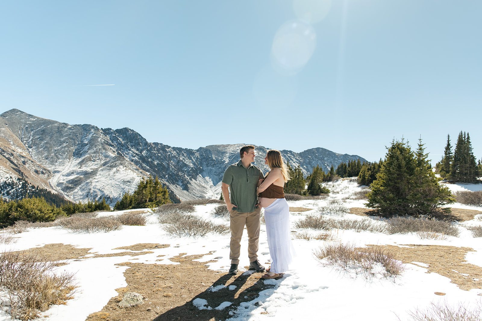 a mom and dad to be stand among some freshly melted snow at Pass Lake for their maternity photos
